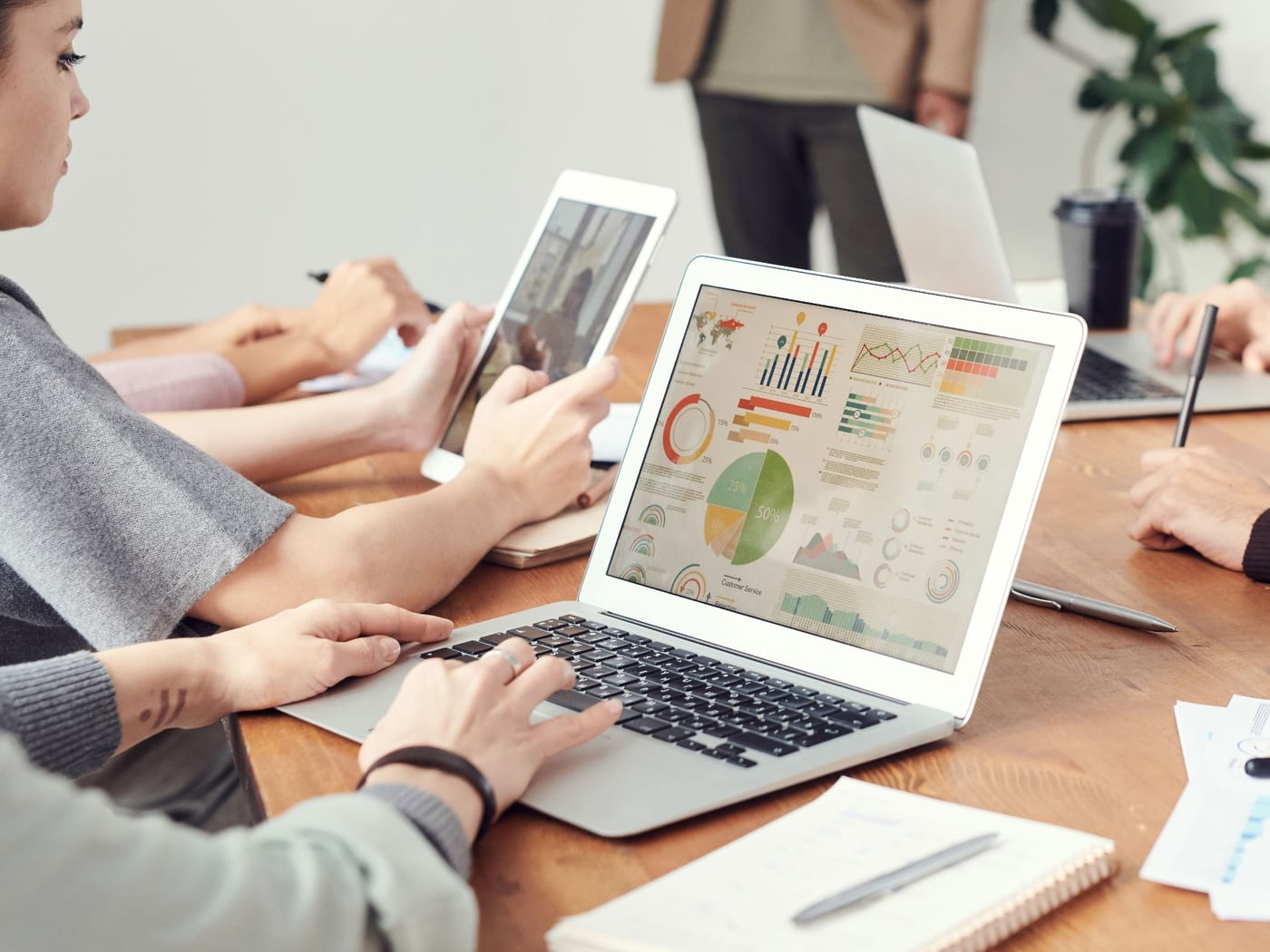 A laptop on a shared table showing a dashboard of charts, with colleagues working either side of it