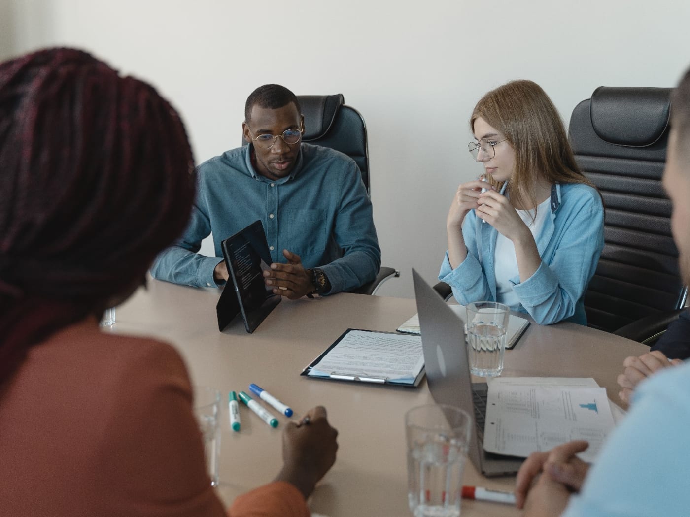 Four people around a meeting table with a tablet, a laptop and printed documents between them