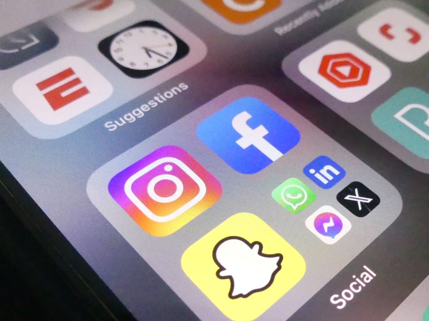A phone screen showing a folder of social apps — Instagram, Facebook, LinkedIn, WhatsApp, X, Messenger and Snapchat